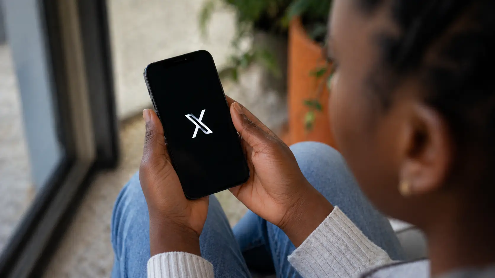 user holding smartphone with X app open on screen in real life setting